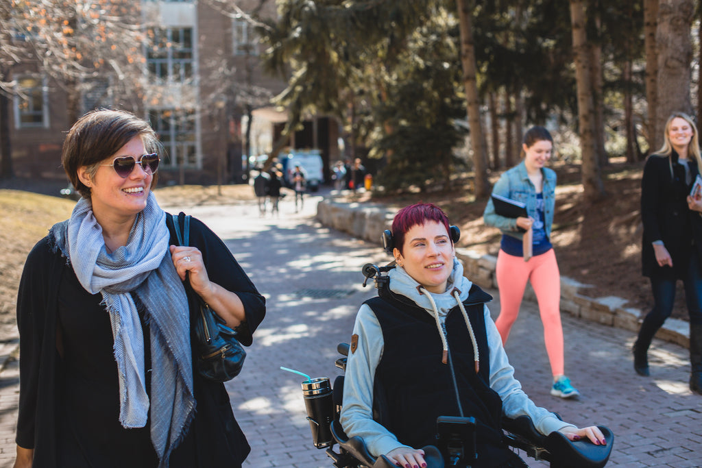 Woman walking next to woman in wheelchair outdoors